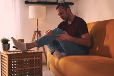 Evdeki koltukta oturan diz ağrısı olan bir adam..