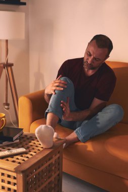 Evdeki koltukta oturan diz ağrısı olan bir adam..