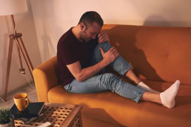 Evdeki koltukta oturan diz ağrısı olan bir adam..