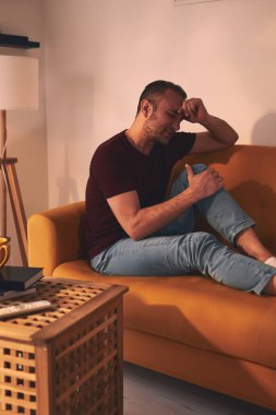 Evdeki koltukta oturan diz ağrısı olan bir adam..