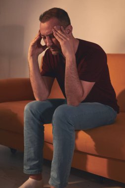 Başı ağrıyan adam evdeki kanepede oturuyor..