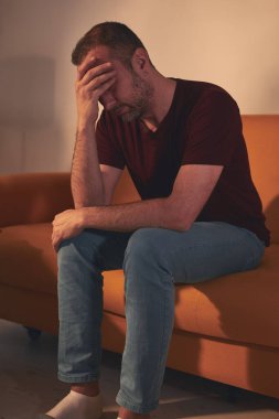 Başı ağrıyan adam evdeki kanepede oturuyor..