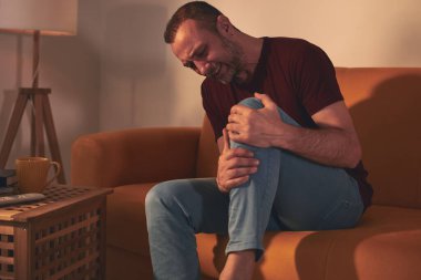 Evdeki koltukta oturan diz ağrısı olan bir adam..