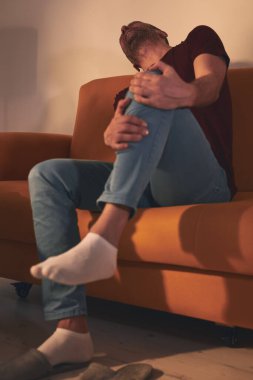 Evdeki koltukta oturan diz ağrısı olan bir adam..