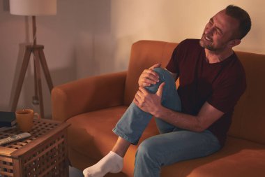 Evdeki koltukta oturan diz ağrısı olan bir adam..