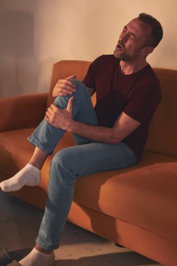 Evdeki koltukta oturan diz ağrısı olan bir adam..