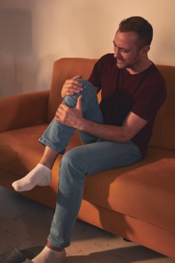 Evdeki koltukta oturan diz ağrısı olan bir adam..