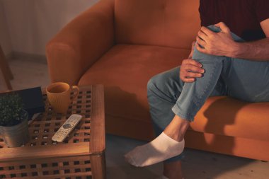 Evdeki koltukta oturan diz ağrısı olan bir adam..