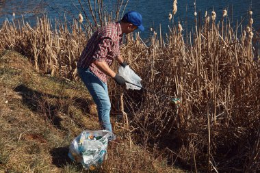 Gönüllü ve çevreci eylemci çöplerle dolu kirli göl kıyılarını temizliyor..
