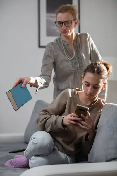 Mother having trouble with a lazy teenager girl at home while playing video games on a smartphone.