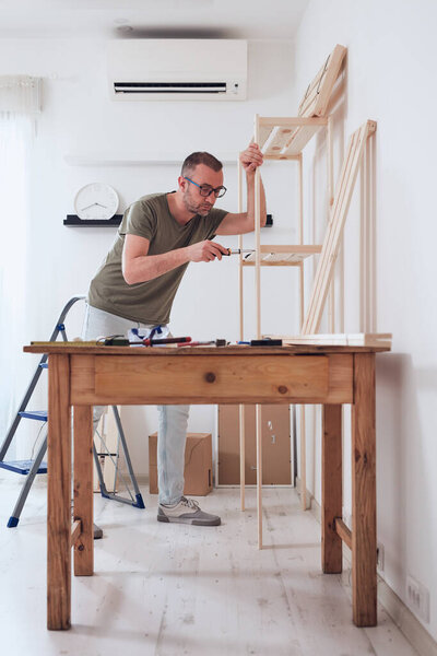 Man assembling new wooden shelf and furniture in the apartment.