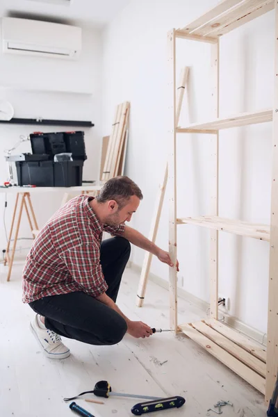 Yeni ahşap bir raf ve mobilya monte eden bir adam..