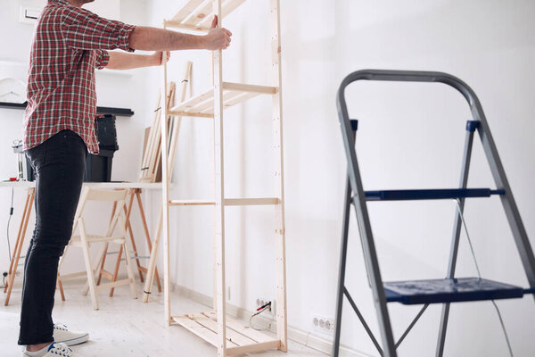 Man assembling new wooden shelf and furniture in the apartment.