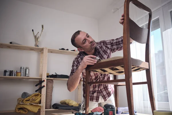 Mobilya onarımı ve restorasyonu için küçük bir ev atölyesinde çalışan bir adam.