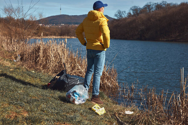 Волонтёр и эколог очищают грязное озеро от мусора.