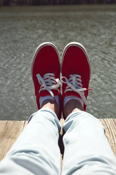 Person in red shoes relaxing on a lake wooden deck.