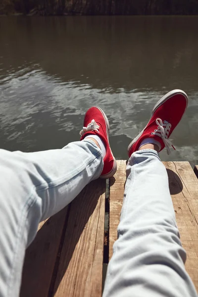 Person in red shoes relaxing on a lake wooden deck.