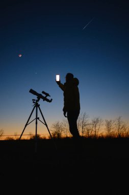 Yıldızlı gökyüzüne bakan astronom gezegenler, kayan yıldızlar ve teleskopla Ay tutulması modern akıllı telefon kullanarak.