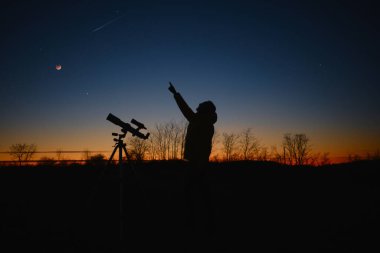 Astronomer looking at the starry skies and crescent Moon with a telescope. clipart