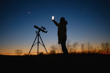 Yıldızlı gökyüzüne bakan astronom gezegenler, kayan yıldızlar ve teleskopla Ay tutulması modern akıllı telefon kullanarak.