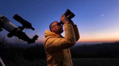 Akşam gökyüzüne bakan amatör astronom gezegenleri, yıldızları, ayı ve diğer gök cisimlerini dürbün ve teleskopla gözlemliyor..