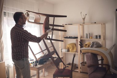 Mobilya onarımı ve restorasyonu için küçük bir ev atölyesinde çalışan bir adam.