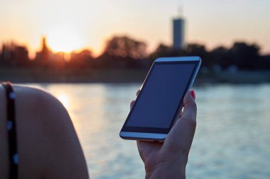 Gün batımında elinde cep telefonu olan bir kadın..