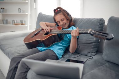 Gitar çalan ve dizüstü bilgisayarda video dersleri izleyen bir çocuk..