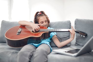 Gitar çalan ve dizüstü bilgisayarda video dersleri izleyen bir çocuk..