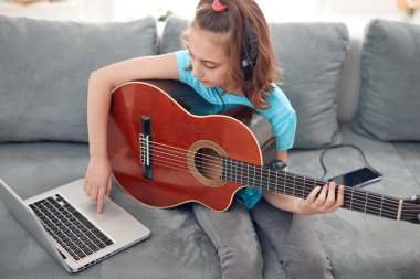 Gitar çalan ve dizüstü bilgisayarda video dersleri izleyen bir çocuk..