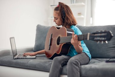 Gitar çalan ve dizüstü bilgisayarda video dersleri izleyen bir çocuk..
