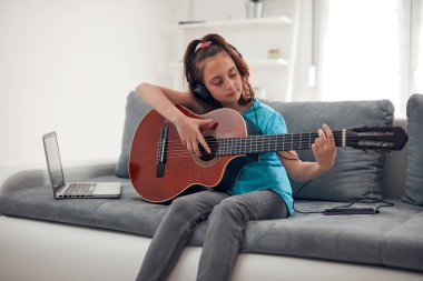 Gitar çalan ve dizüstü bilgisayarda video dersleri izleyen bir çocuk..