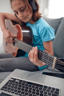 Gitar çalan ve dizüstü bilgisayarda video dersleri izleyen bir çocuk..