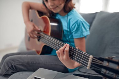 Gitar çalan ve dizüstü bilgisayarda video dersleri izleyen bir çocuk..