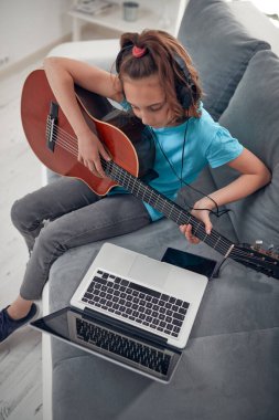 Gitar çalan ve dizüstü bilgisayarda video dersleri izleyen bir çocuk..