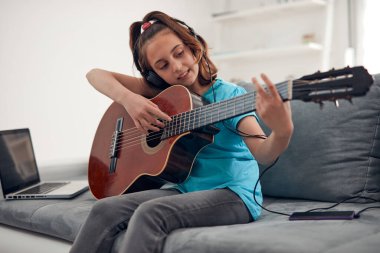 Gitar çalan ve dizüstü bilgisayarda video dersleri izleyen bir çocuk..