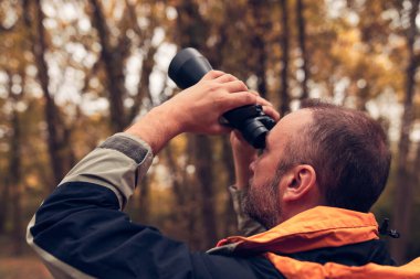 Dürbün ve kamera kullanan adam doğada kuşları ve hayvanları izliyor..