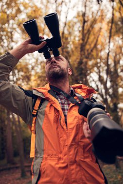 Dürbün ve kamera kullanan adam doğada kuşları ve hayvanları izliyor..