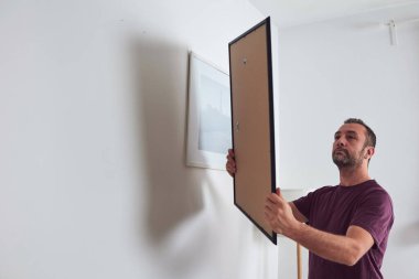 Duvara resim asan, evi temizleyen ve dekore eden bir adam..