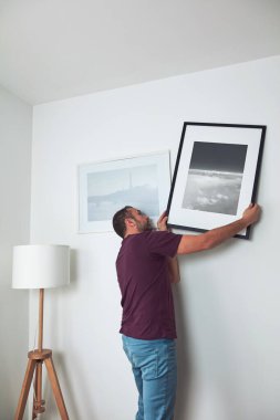 Duvara resim asan, evi temizleyen ve dekore eden bir adam..
