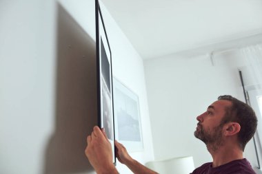 Duvara resim asan, evi temizleyen ve dekore eden bir adam..