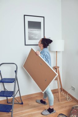 Duvara resim asan, temizlik yapan, evini dekore eden bir kadın..