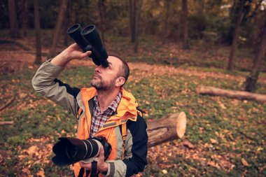 Dürbün ve kamera kullanan adam doğada kuşları ve hayvanları izliyor..