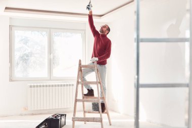 Yeni bir evde çalışan merdivenli tamirci elektrikçi..