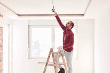Yeni bir evde çalışan merdivenli tamirci elektrikçi..