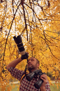 Dürbün ve kamera kullanan adam doğada kuşları ve hayvanları izliyor..