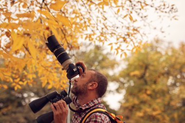 Dürbün ve kamera kullanan adam doğada kuşları ve hayvanları izliyor..