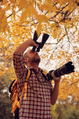 Dürbün ve kamera kullanan adam doğada kuşları ve hayvanları izliyor..