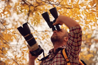 Dürbün ve kamera kullanan adam doğada kuşları ve hayvanları izliyor..