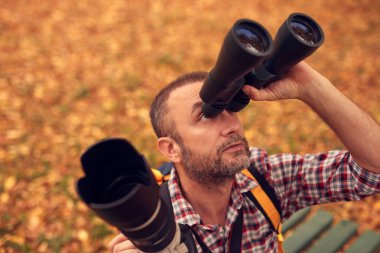 Dürbün ve kamera kullanan adam doğada kuşları ve hayvanları izliyor..